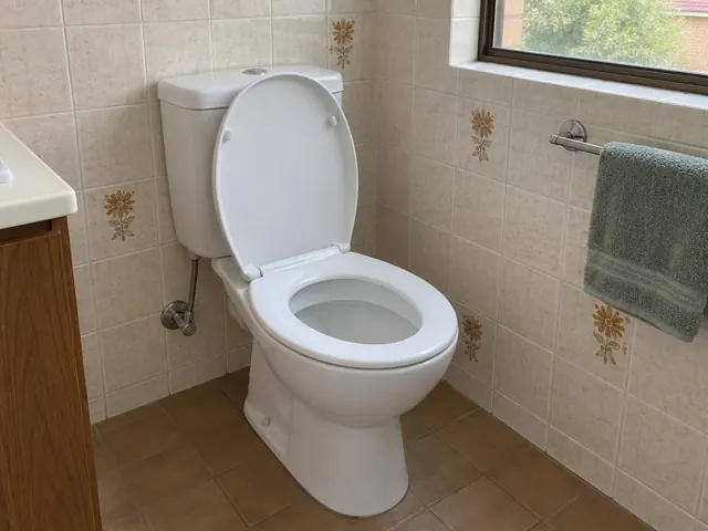 Clean white toilet in a tiled bathroom beside a window and towel rail in St Ives