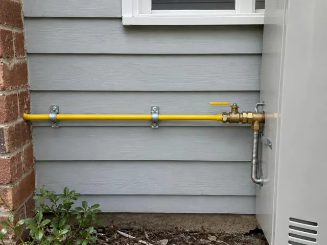 Yellow gas pipe and valve mounted on a grey weatherboard exterior wall in Pymble